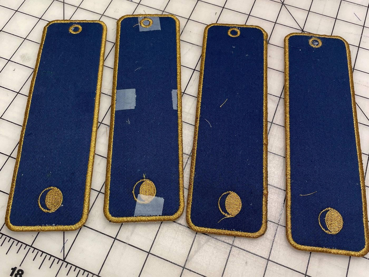 The backs of the same four bookmarks: plain navy twill inside the gold border, each with a small gold moon embroidered near the bottom.
