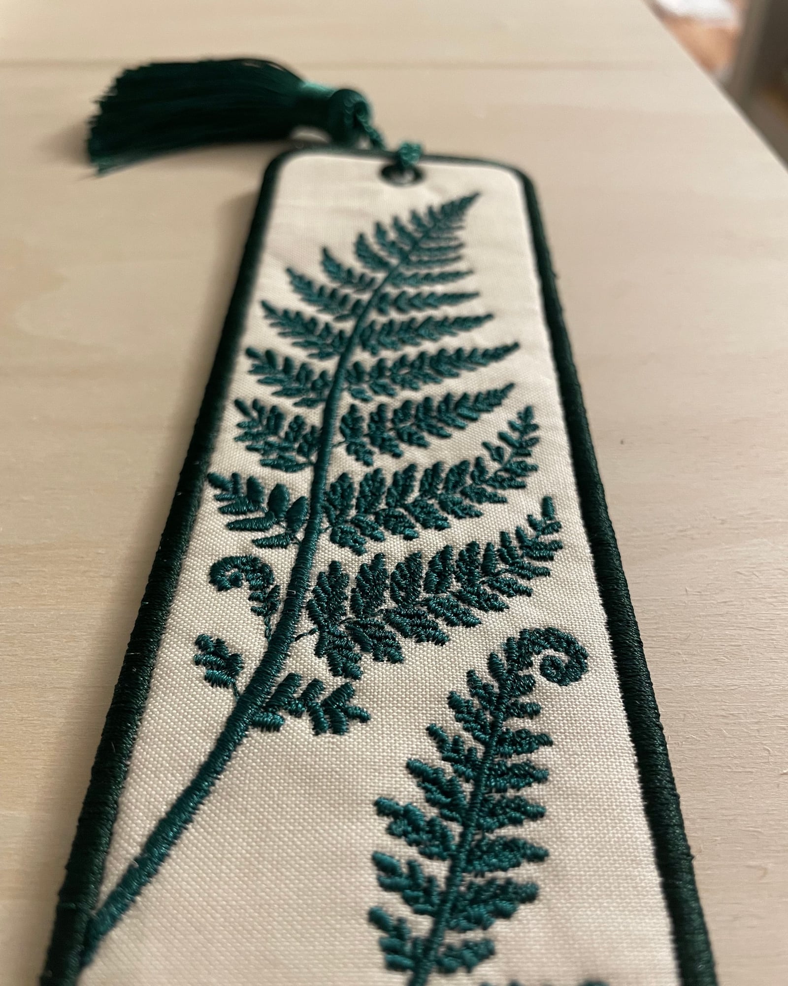 A close-up of the bookmark at an angle, showing the stitched fern leaves and a curled fiddlehead.